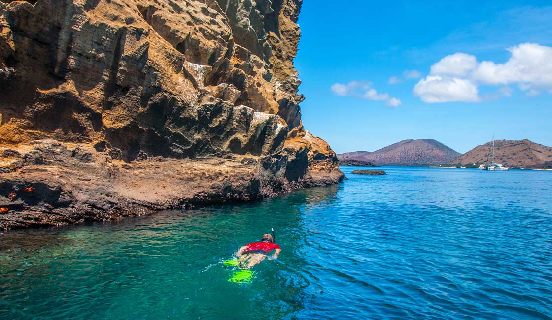 Galapagos'ta büyük bir kaya oluşumunun yanında şnorkelle yüzen kişi