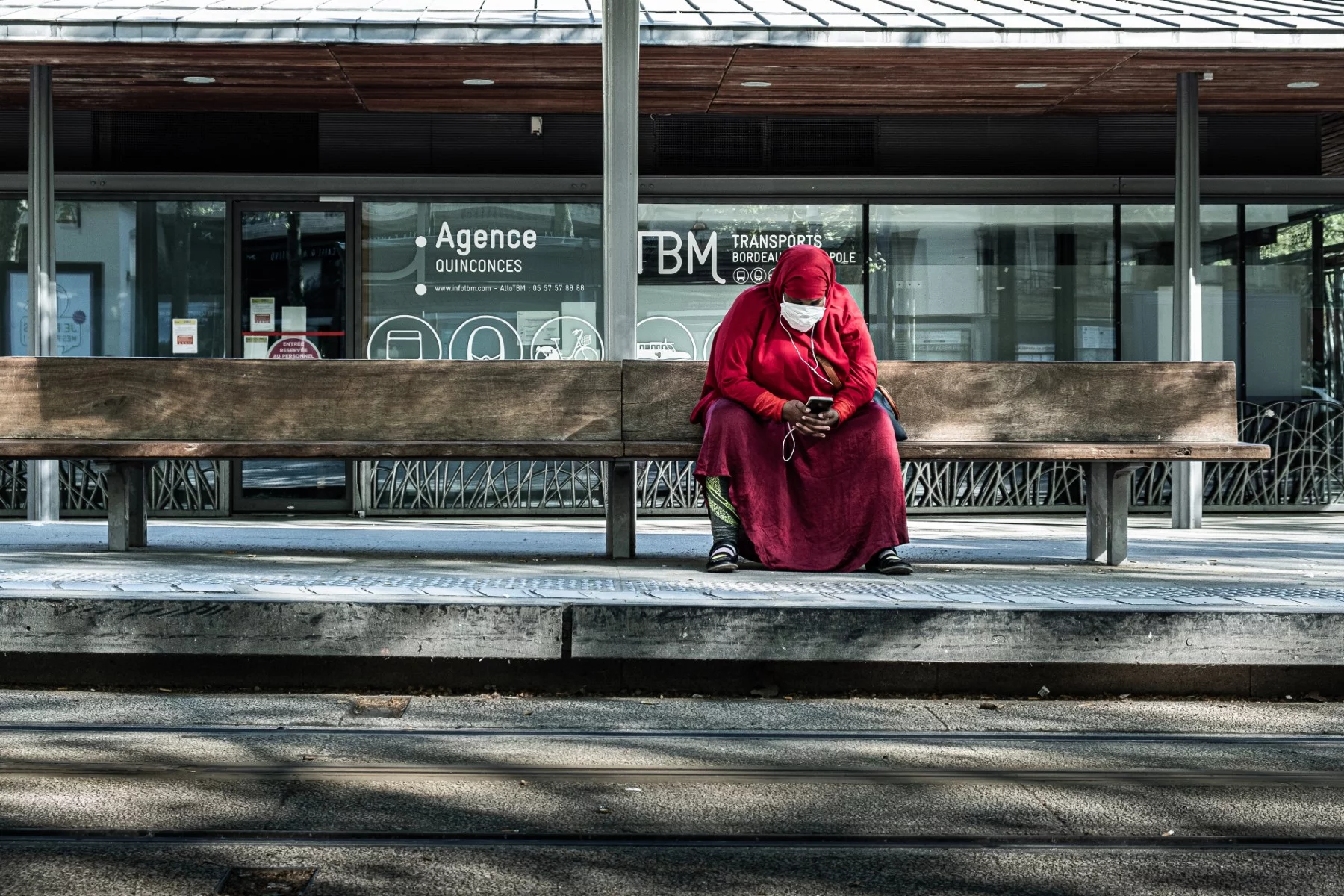 Kırmızı burkalı bir bayan toplu taşımada beklerken telefonunda müzik dinliyor.