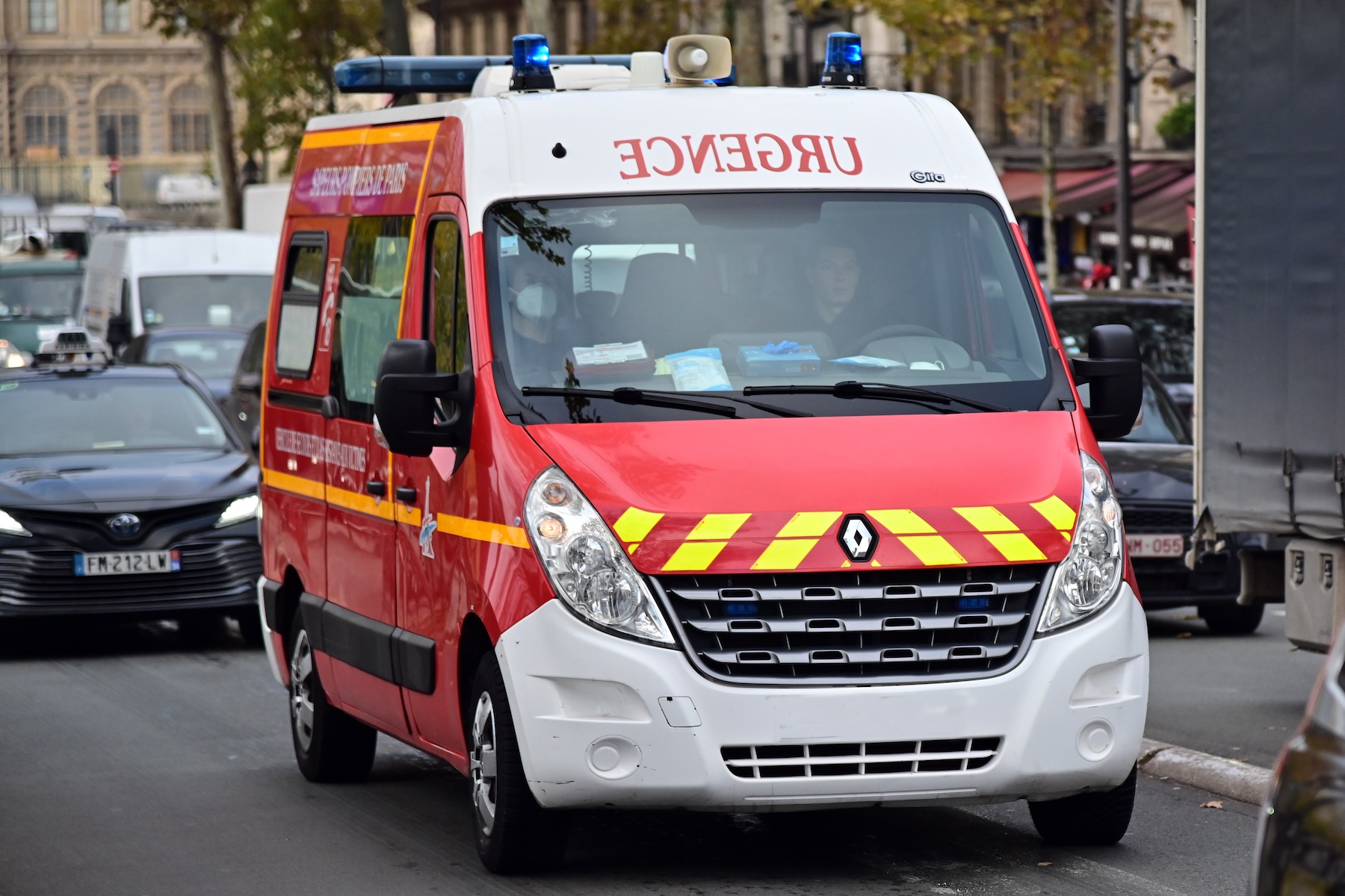Bir ambulans, mavi acil durum ışıkları açıkken yoğun bir Paris sokağında ilerliyor
