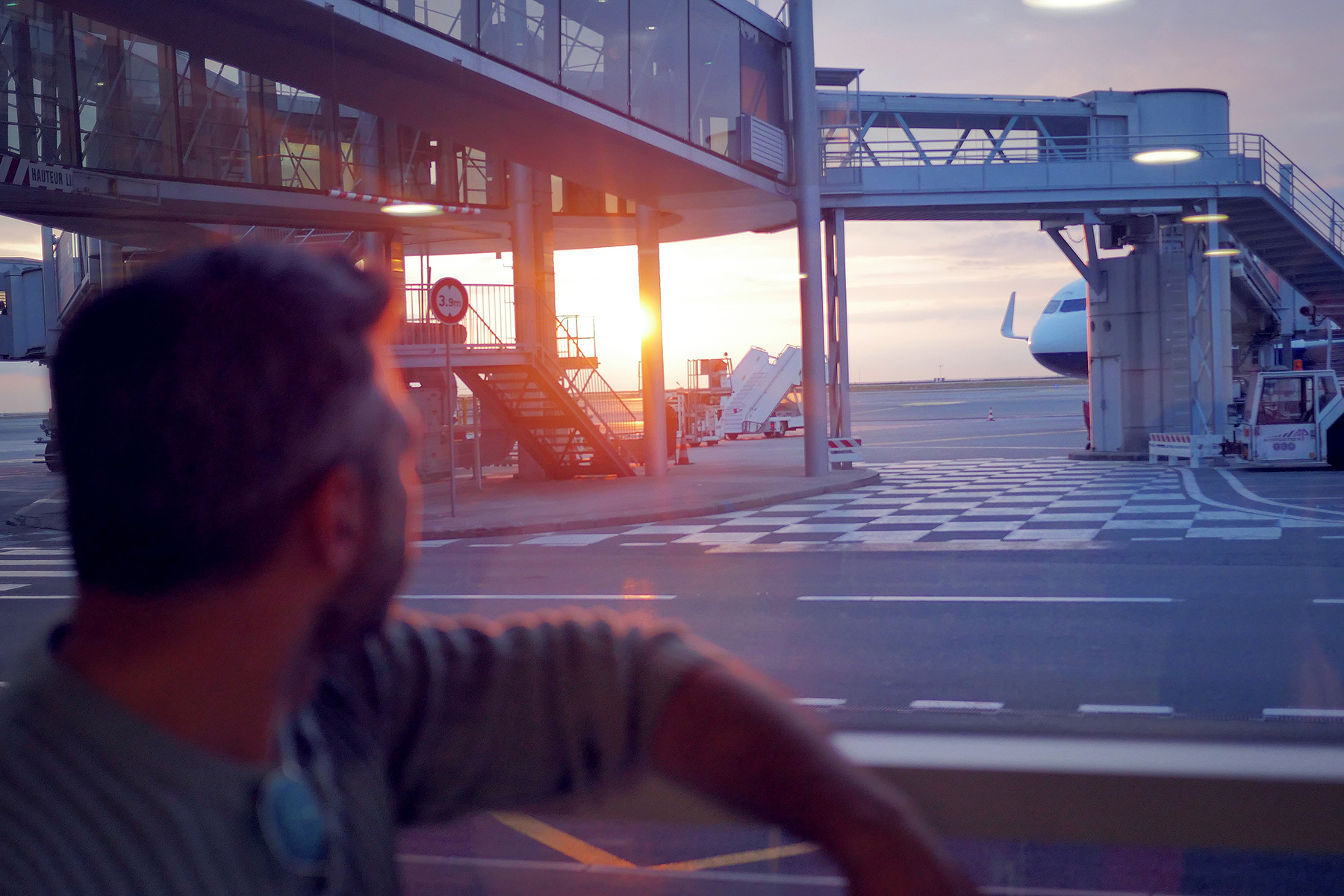 Gün batımında havaalanı penceresinden uçaklara bakan adam