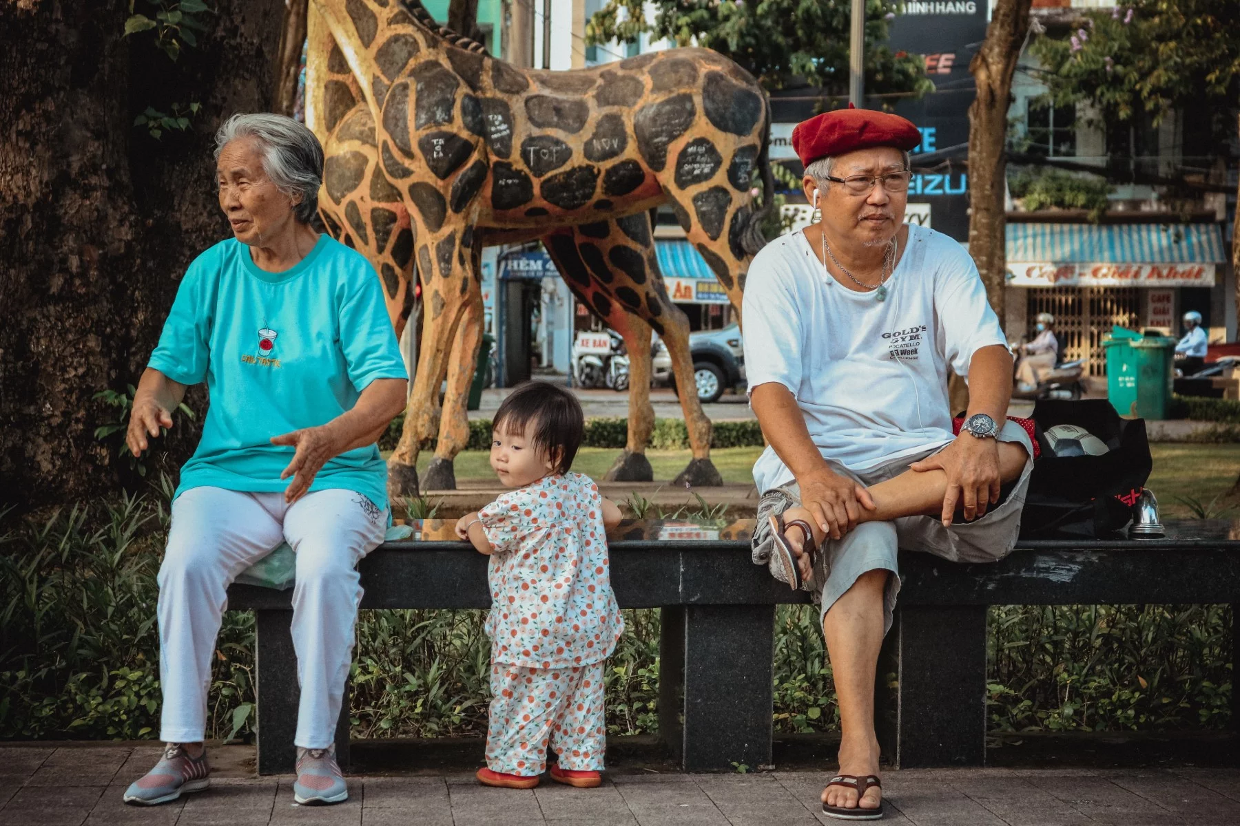 Hayvanat bahçesinin yanında büyükanne ve büyükbabasının arasında duran bir yürümeye başlayan çocuk.
