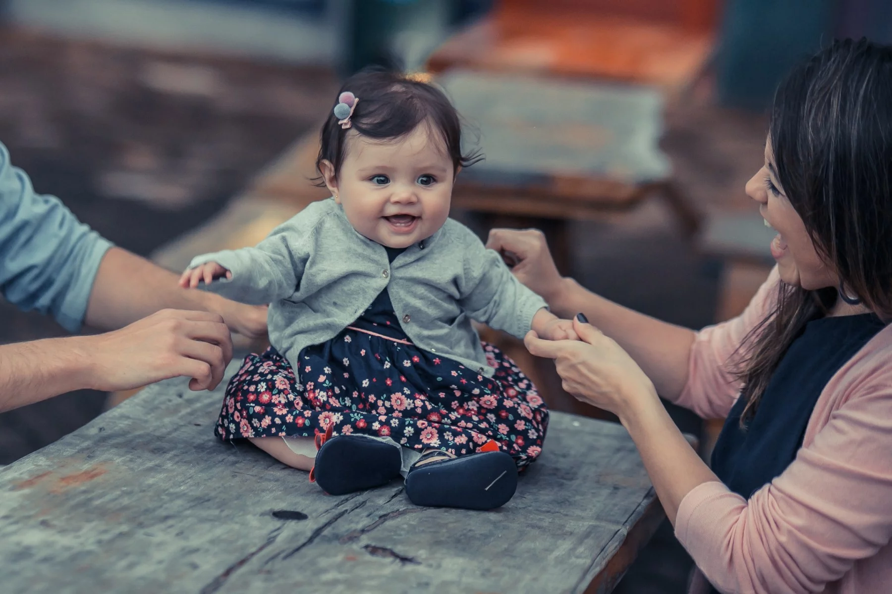 Bir masada oturan bir kız bebek, gülen annesi onu tutarken gülüyor.